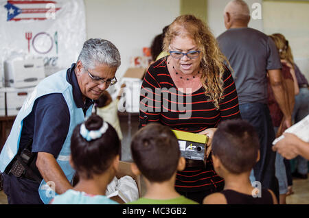 HUMACAO, Puerto Rico, 12. Januar 2018 - EIN FEMA-Mitarbeiter zusammen mit der Community Leader neue Schuhe für Kinder in Punta Santiago verteilen. Die FEMA geholfen, die Spende organisieren über 150 Paar Schuhe der Kinder auf Hurrikan Maria Überlebenden zu liefern. Stockfoto