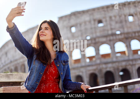 Brunette in Kleidung und Denim mit Telefon und unter selfie auf Hintergrund Kolosseum im Sonnenlicht. Stockfoto