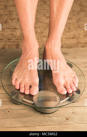 Man steht auf der Waage. Männliche Füße auf Glasmaßstäbe und Holzboden Stockfoto