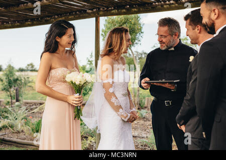 Lächelnd Braut im Gespräch mit Priester nach der Trauung unter Hochzeit arch. Schöne Hochzeitszeremonie im Freien. Stockfoto