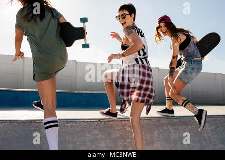 Lachende Frau Klettern ein Skateboard Rampe mit Freunden. Gruppe von Mädchen, die eine großartige Zeit bei Skate Park. Stockfoto