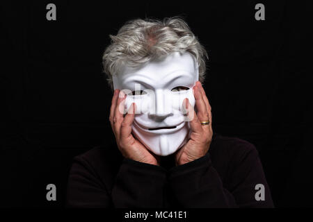 Grauhaariger Mann in anonymen Maske sein Gesicht in seinen Händen halten Stockfoto