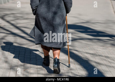 An einem sonnigen Tag eine alte Frau auf der Straße mit walking stick Walking. Schatten der Frau ist sichtbar auf dem Bürgersteig. Ansicht von der Rückseite. Stockfoto