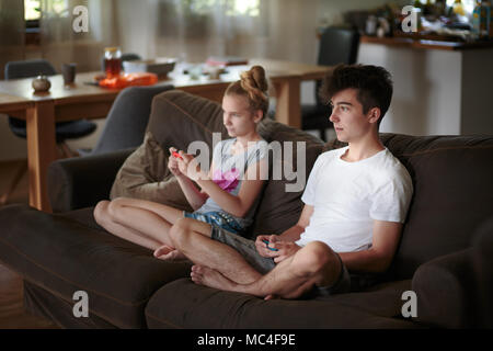 Konzentrierte sich Jungen und Mädchen spielen Videospiele auf dem Sofa zu Hause sitzen Stockfoto