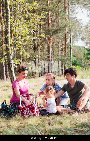 Familie Urlaub verbringen die Zeit zusammen mit einem Snacks auf ein Picknick sitzen auf Decke auf Gras im Wald an einem sonnigen Tag im Sommer Stockfoto