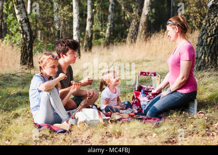 Familie Urlaub verbringen die Zeit zusammen mit einem Snacks auf ein Picknick sitzen auf Decke auf Gras im Wald an einem sonnigen Tag im Sommer Stockfoto