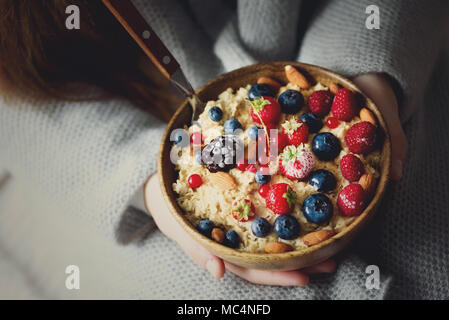 Frau Hände, die haferflocken Porridge mit gefrorenen Früchten, Mandeln in Houten. Banner. Gesundes Frühstück. Sauber Essen, detox Diät. Vegetarische, Raw, vegan Konzept Stockfoto