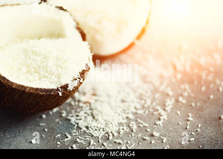 Coconut fuit Hälften mit Kokos Späne auf grauem Beton Hintergrund. Copyspace Stockfoto