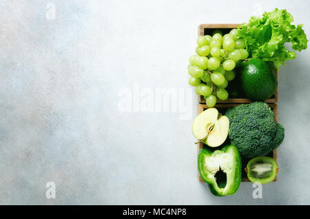 Organische grünes Gemüse und Früchte auf grauem Hintergrund. Kopieren Sie Raum, Flach, Ansicht von oben. Grüner Apfel, Salat, Zucchini, Gurke, Avocado, Kale, Kalk, Kiwi, Trauben, Bananen, Brokkoli Stockfoto