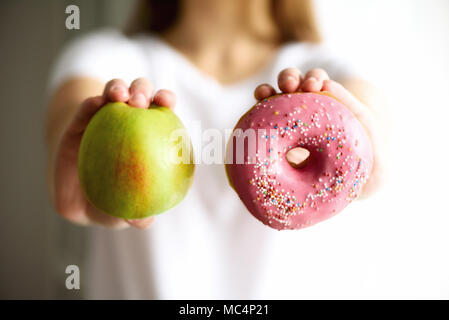 Junge Frau im weißen T-Shirt Wahl zwischen grüner Apfel oder Junk Food, Donut. Gesunde, saubere detox Essen Konzept. Vegetarisch, vegan, raw-Konzept. Platz kopieren Stockfoto