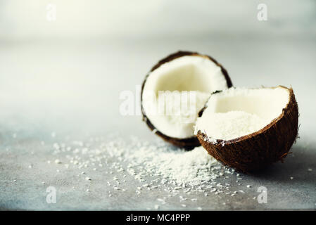 Coconut fuit Hälften mit Kokos Späne auf grauem Beton Hintergrund. Copyspace Stockfoto