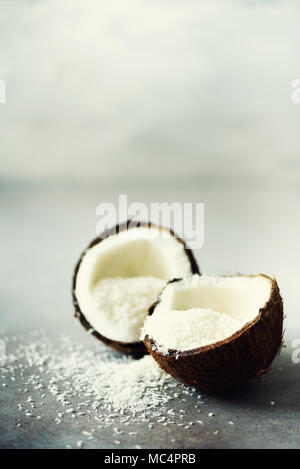 Coconut fuit Hälften mit Kokos Späne auf grauem Beton Hintergrund. Copyspace Stockfoto