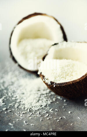 Coconut fuit Hälften mit Kokos Späne auf grauem Beton Hintergrund. Copyspace Stockfoto