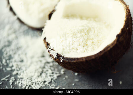 Coconut fuit Hälften mit Kokos Späne auf grauem Beton Hintergrund. Copyspace Stockfoto