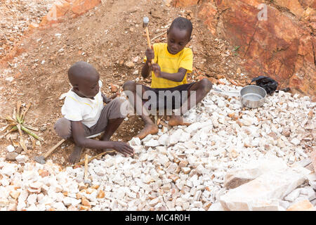 Lugazi, Uganda. 18. Juni 2017. Ugandische Jungen brechen Steine in kleine Platten für den Verkauf an ihre Vorarbeiter. Im Grunde Kinderarbeit. Stockfoto