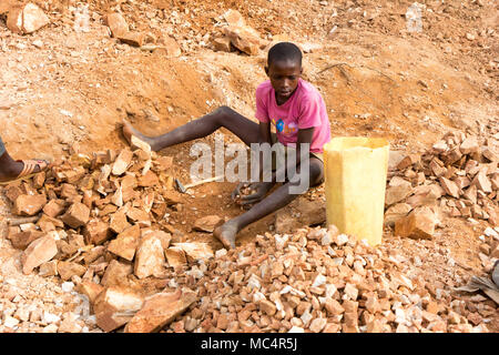 Lugazi, Uganda. 18. Juni 2017. Eine ugandische Boy brechen Steine in kleine Platten für seinen Meister. Im Grunde Kinderarbeit. Stockfoto