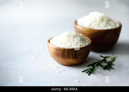 Weißen organischen Jasmin Reis in Houten und Rosmarin auf Licht konkreten Hintergrund. Food Ingredients. Platz kopieren Stockfoto