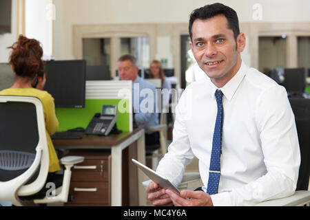 Portrait von Geschäftsmann mit digitalen Tablet Sitzen im hektischen modernen Büro Stockfoto