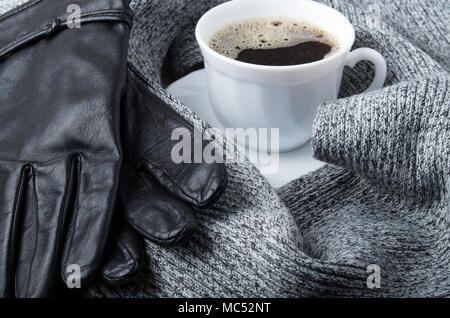 Grauer Wolle Schal und Handschuhe durch eine heiße Tasse Kaffee mit geringer Tiefenschärfe umgeben Stockfoto