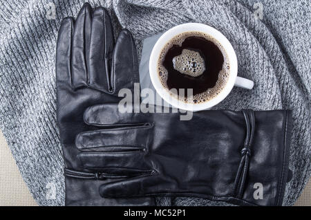 Draufsicht auf eine weiße Tasse Kaffee, einen grauen Schal und schwarze Handschuhe sind aus Leder gefertigt Stockfoto