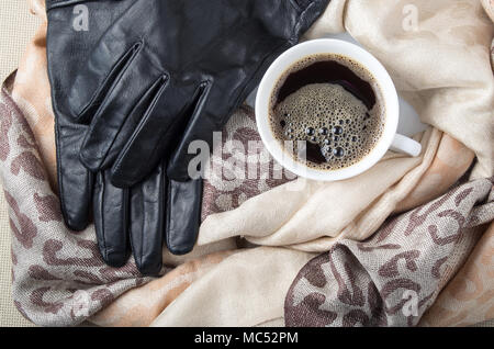 Blick von oben auf eine weiße Tasse Kaffee in die Falten des Schals und schwarzem Leder Handschuhe Stockfoto