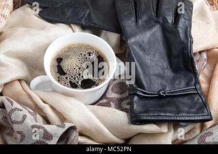 Blick von oben auf eine weiße Tasse Kaffee in die Falten des weiblichen Schal und Handschuhe aus schwarzem Leder Stockfoto