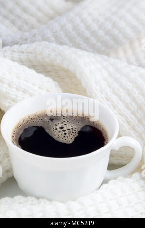Weiße Tasse mit heißem Kaffee in einem weißen Wollschal mit geringer Tiefenschärfe gewickelt. Stockfoto