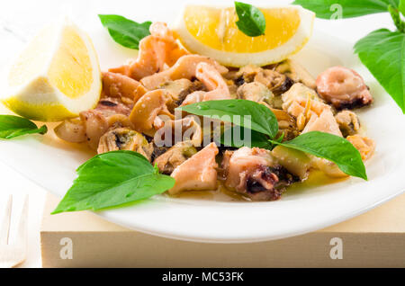 Salat von blanchierte Meeresfrüchte auf einem weißen Teller. Muscheln und Tintenfisch, dekoriert mit Gruenen und Zitrone. Stockfoto