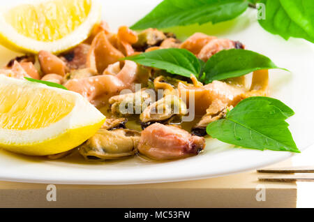 Salat von blanchierte Meeresfrüchte auf einem weißen Teller close-up. Muscheln und Tintenfisch, dekoriert mit Gruenen und Zitrone. Stockfoto