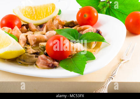 Salat von blanchierte Stücke von Meeresfrüchten auf einer weißen Platte close-up. Muscheln und Tintenfisch, dekoriert mit grünen, Kirsch und Zitrone. Stockfoto