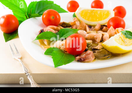 Salat von blanchierte Stücke von Meeresfrüchten auf einer weißen Platte close-up. Muscheln und Tintenfisch, dekoriert mit grünen, Kirsch und Zitrone. Stockfoto