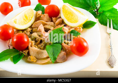 Salat von blanchierte Stücke von Meeresfrüchten auf einer weißen Platte close-up. Muscheln und Tintenfisch, dekoriert mit grünen, Cherry Tomaten und Zitronen mit Stockfoto