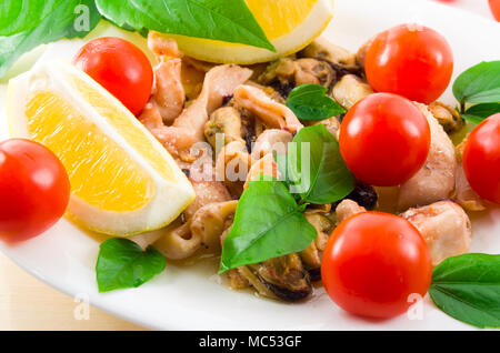 Salat von blanchierte Stücke von Meeresfrüchten auf einer weißen Platte close-up. Muscheln und Tintenfisch, dekoriert mit grünen, Cherry Tomaten und Zitronen mit Stockfoto