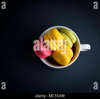 Mehrfarbige gebackenen Kuchen von Mandeln Mehl macarons in eine weiße Keramik Tasse auf einem schwarzen Hintergrund, Ansicht von oben Stockfoto