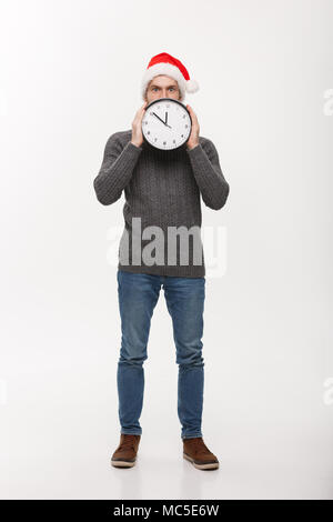 Urlaub Konzept - Junge stattlicher Bart Mann hinter weißen Uhr über weiße studio Hintergrund versteckt Stockfoto