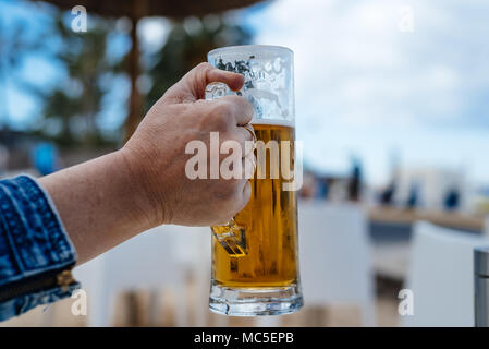 Hand der Frau mit einem Pint Bier gegen verwackelte Sommer Hintergrund Stockfoto