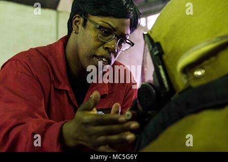 180403-N-ist 471-0215 Yokosuka, Japan (Apr. 3, 2018) Schäden Controlman 1. Klasse Nakia Bugg, von Cobb County, Georgia, unterstützt eine Sailo auf die marine Vorwärts - bereitgestellt Flugzeugträger USS Ronald Reagan (CVN 76) Für eine ordnungsgemäße Dichtung auf eine Brandbekämpfung Maske während der Ausbildung an der Yokosuka Brandbekämpfung und Beschädigungen der Anlage zu prüfen. Ronald Reagan, das Flaggschiff der Carrier Strike Group 5, bietet eine Bekämpfung bereit, Kraft, schützt und verteidigt die kollektive maritime Interessen seiner Verbündeten und Partnern in der Indo-Asia-Pazifik-Region. (U.S. Marine Foto von Massenkommunikation Spezialist Stockfoto