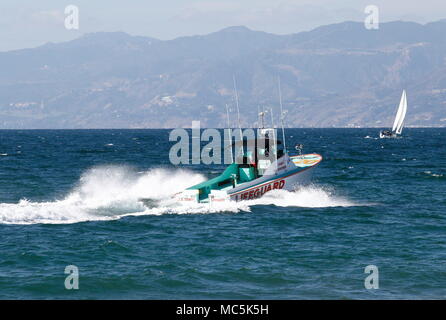 LA Feuerwehr Rettungsschwimmer Rettungsboot bei einer Geschwindigkeit auf dem Pazifik mit den Hügeln von Santa Barbara und eine kleine Yacht im Hintergrund. Stockfoto