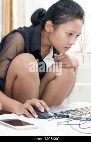 Eine junge Frau, die auf ihrem Laptop auf dem Bett. Eine nachdenkliche Mädchen schreibt auf Computer im Schlafzimmer. Stockfoto