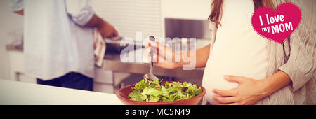 Das zusammengesetzte Bild der schwangeren Frau mischen einen Salat in der Küche Stockfoto