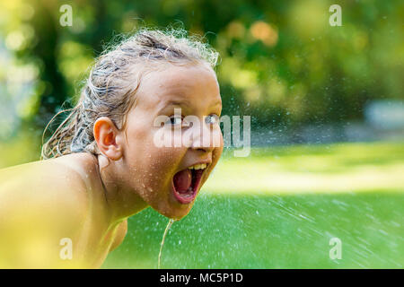 Junge Mädchen fangen Tropfen Wasser aus dem Garten. Stockfoto