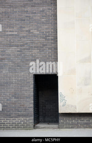 Minimalistische urbane Architektur mit einem starken Kontrast zwischen dunklem Ziegelwerk und heller Steinfassade, mit einer kleinen eingelassenen Eingangstür und dezentem graff Stockfoto