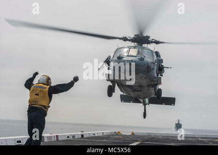 Pazifik (31. März 2018) der Luftfahrt Bootsmann Mate (Handling) Airman Frederick Medina, ein Eingeborener von Delano, Kalifornien, leitet eine MH-60S Sea Hawk, der "Blackjacks" der Hubschrauber Meer Combat Squadron (HSC) 21, auf dem Flugdeck von San Antonio - Klasse amphibious Transport dock USS Anchorage LPD (23), während eine amphibische Squadron und 13 Marine Expeditionary Unit (MEU) Integration (PMINT) Übung befestigt. PMINT ist ein Training Entwicklung zwischen Essex Amphibious Ready Gruppe und 13 MEU, Matrosen und Marines als zusammengehörige Einheit in der Vorbereitung für die bevorstehende Bereitstellung zu trainieren. Stockfoto