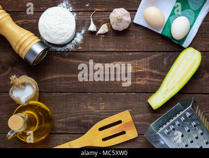 Die Zutaten und Werkzeuge für das Kochen Pfannkuchen aus Zucchini auf einem dunklen Hintergrund. Ansicht von oben. In der Mitte des freien Platz für Text Stockfoto