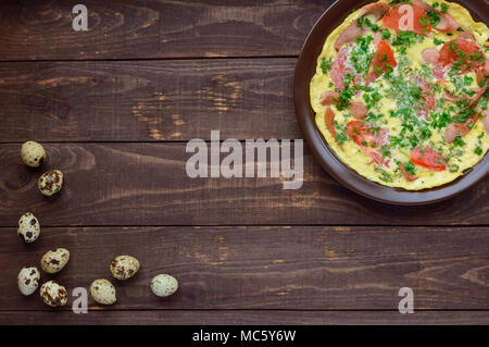 Omelette mit Wurst und frischen Tomaten und Kräutern auf einem Ton Platte und Wachteleier. Die Ansicht von oben. Frühstück Stockfoto