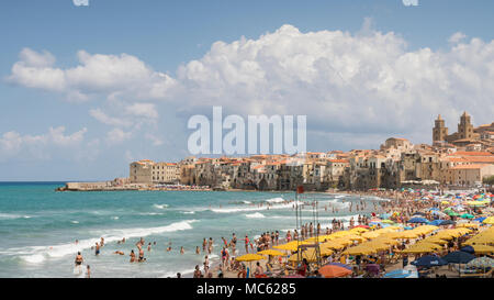 Cefalu, Sizilien, Italien. Sonnenschirme füllen Sie den Sandstrand an einem sonnigen Tag im August mit Massen von Menschen im Meer schwimmen, der gelbe Abschnitt ist eine bezahlte Stockfoto