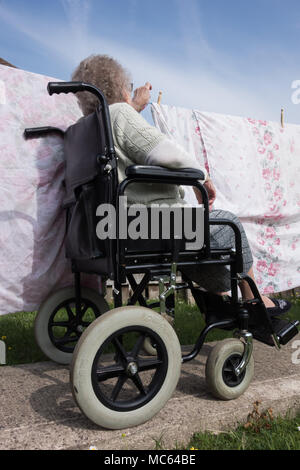 90 Jahre alte Frau im Rollstuhl helfende Pflegerin (ihr Sohn) hängt waschen an der Linie. GROSSBRITANNIEN Stockfoto