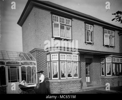 AJAXNETPHOTO. 1910 (CA.). STANDORT UNBEKANNT. - FAMILIE SNAPSHOT - FRAU SCHIEBEN KINDERWAGEN MIT EINEM KIND VOR EINEM GROSSEN HAUS MIT FENSTER IN DER BUCHT UND EINEM WINTERGARTEN AUS GLAS. FOTOGRAF:UNBEKANNT © DIGITAL IMAGE COPYRIGHT AJAX VINTAGE PICTURE LIBRARY SOURCE: AJAX VINTAGE PICTURE LIBRARY COLLECTION REF:181004 06 Stockfoto