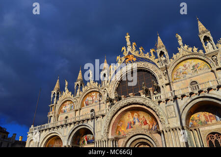 Schöne gotische und byzantinischen Fassade der Basilika von St. Markus in Venedig glänzt bei Sonnenuntergang mit bewölktem Himmel Stockfoto