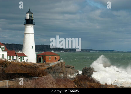 Sonne bricht durch Gewitterwolken als riesige Wellen auf schroffe Felsen beleuchtete Portland Head Lighthouse in Maine zu brechen, während des späten Winters Flut. Stockfoto